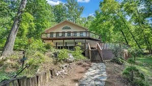 Une cabane en bois à deux étages, dotée d’un balcon et entourée d’une forêt dense.