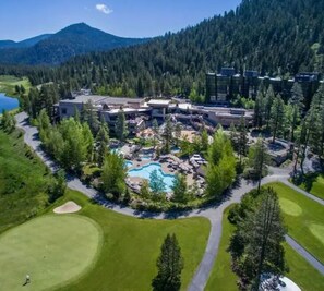 A golf course with a swimming pool and a building complex surrounded by forested hills.