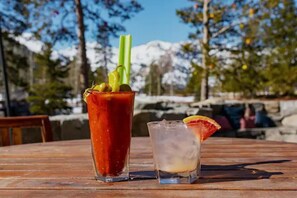 Two drinks on a wooden table with a mountainous background.