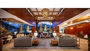 A spacious lobby with a large chandelier, seating areas, and a view of snow-capped mountains through large windows.