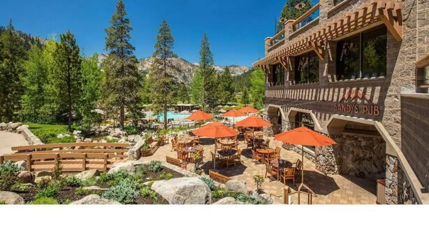 A patio area with outdoor seating and umbrellas, surrounded by a mountainous landscape and a pool.