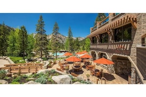 Un patio con mobiliario exterior y sombrillas, rodeado de un paisaje montañoso y una piscina.