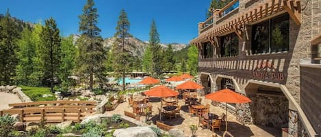 A patio area with outdoor seating and umbrellas, surrounded by a mountainous landscape and a pool.