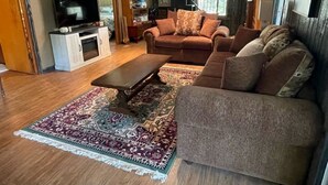Ein gemütliches Wohnzimmer mit einer Couch, einem Couchtisch und einem Fernseher auf einem Schrank. Eine Treppe führt zu einer oberen Ebene.