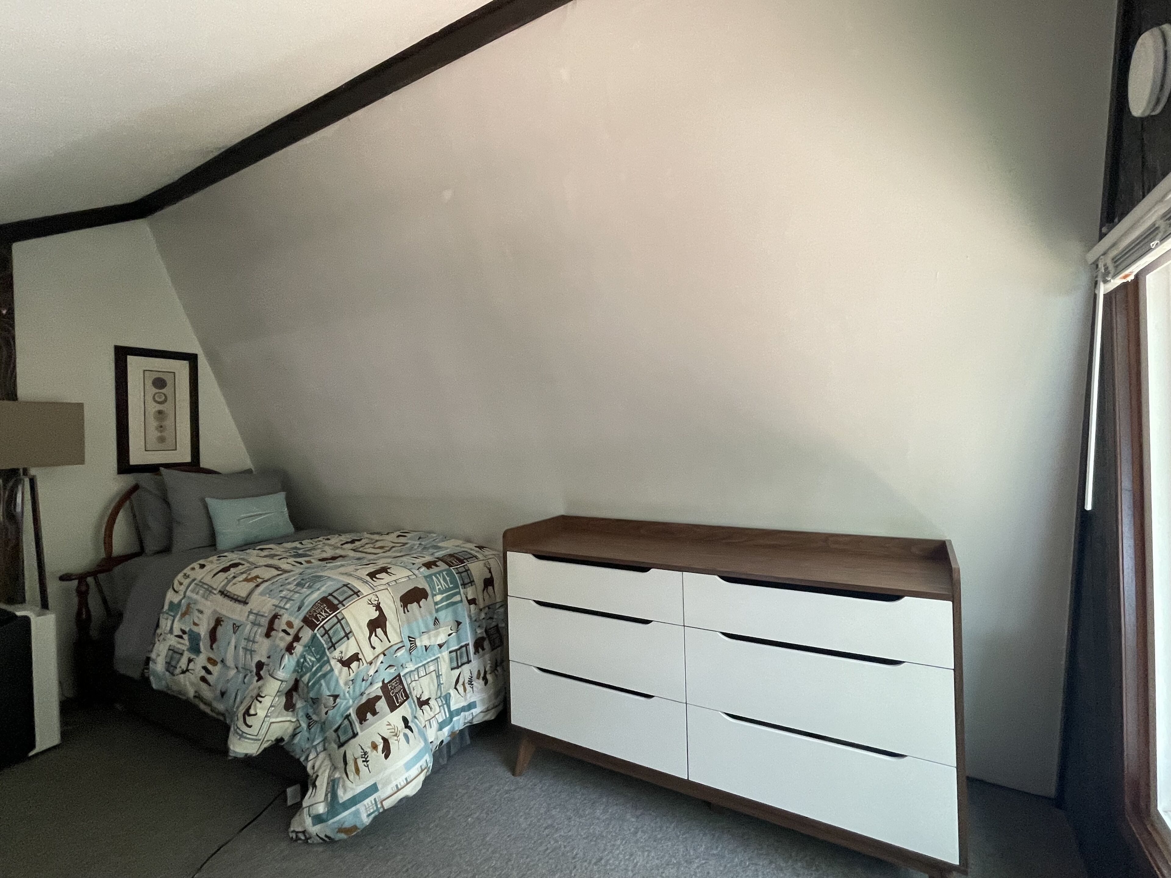 A bedroom with a bed, a white dresser, a framed picture on the wall, and a window.