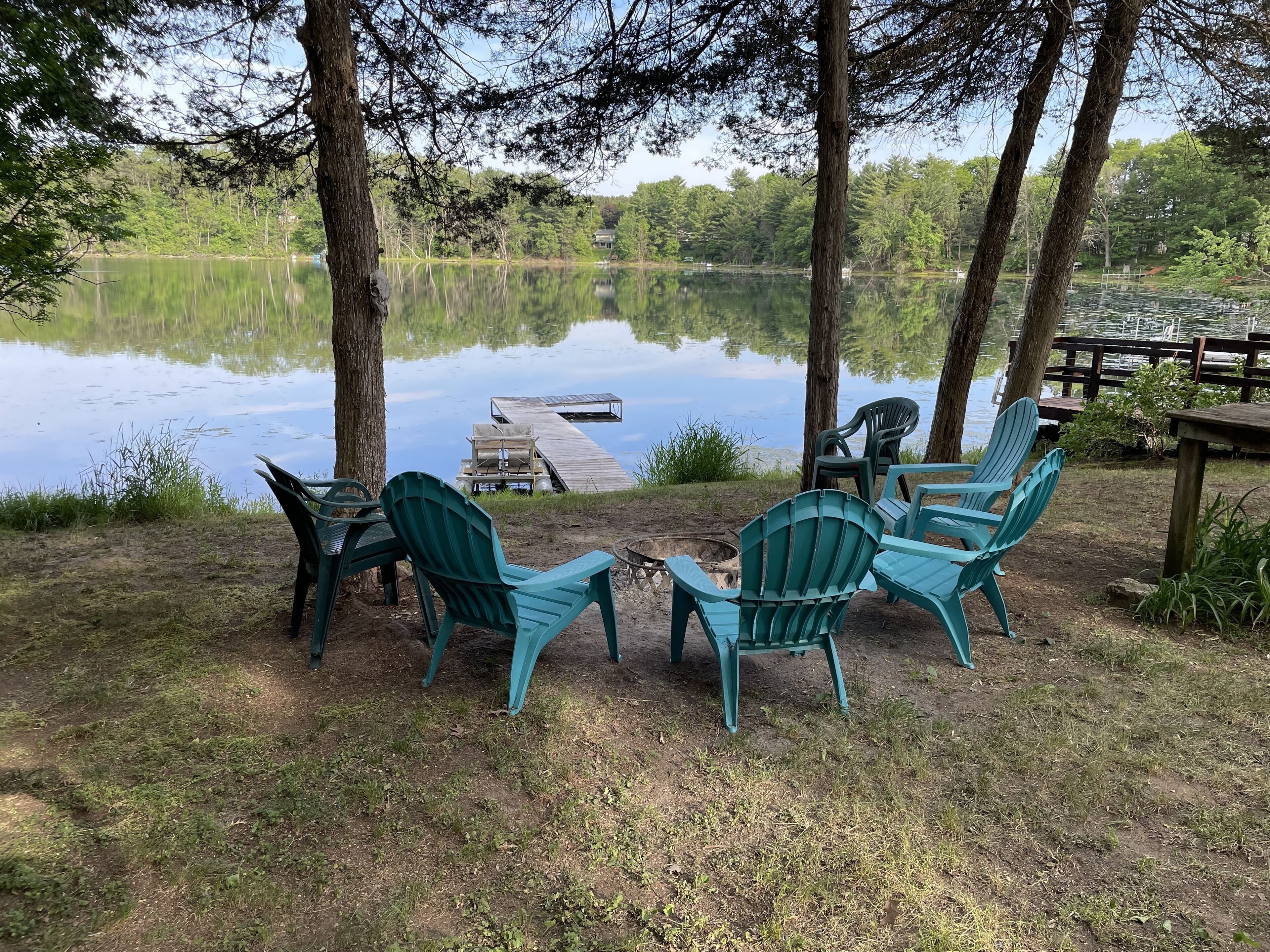 A lakeside seating area with Adirondack chairs and a dock extending into the water.