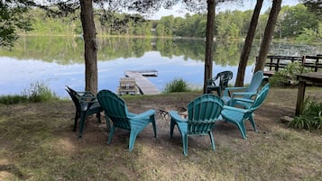 A lakeside seating area with Adirondack chairs and a dock extending into the water.