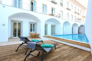 A poolside area with wooden flooring, lounge chairs, and a small table with chairs. - Salty Spot Apartment (Faro)