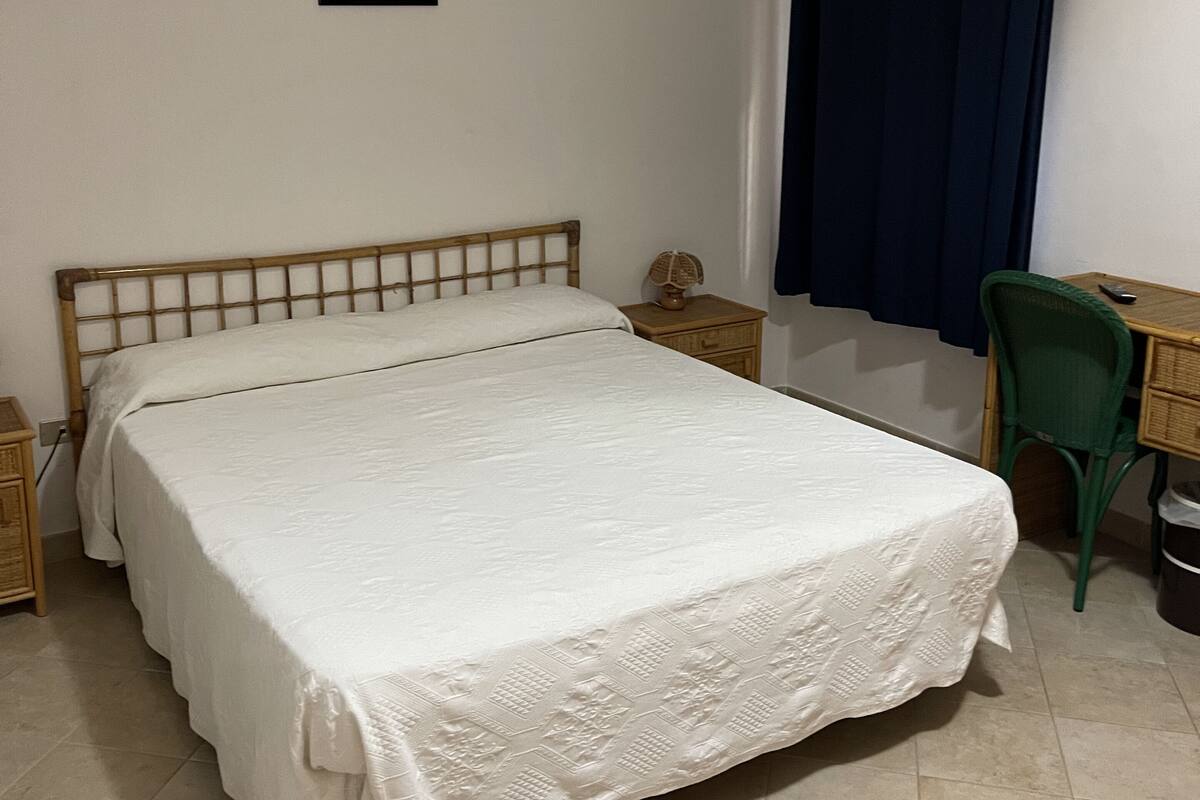 A bedroom with a bed, a desk, a chair, a picture on the wall, and a window with curtains.