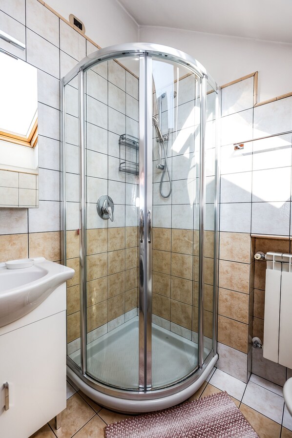 A modern bathroom with a glass-enclosed shower, a white sink, and a beige tiled floor.