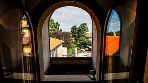 Vista a través de una ventana con marco metálico y cristal, mostrando un edificio con tejado de tejas y un árbol al fondo.