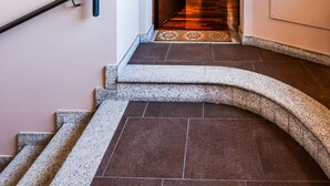 Una escalera curva con barandilla, que conduce a una habitación con una puerta de madera y un suelo con estampado.