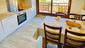 A compact kitchen with modern appliances, a dining area with a table and chairs, and a balcony with a view.