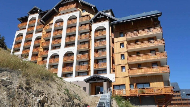 A multi-story hotel with balconies, a staircase leading to the entrance, and a clear sky.