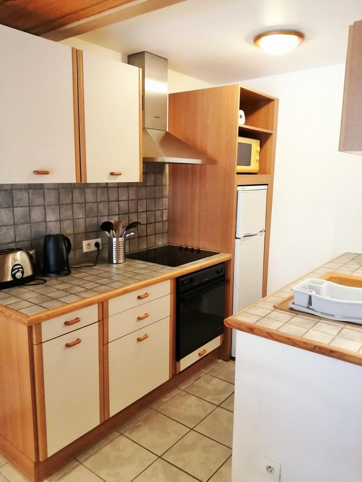 Una cucina compatta con mobili in legno, un fornello nero, un forno a microonde e un tostapane.