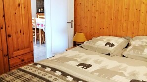 A bedroom with a wooden paneled wall, a bed with a patterned duvet, and a door leading to a dining area. - 100m from ski slopes, 3rd floor, balcony, tv, ski locker, 42m², Les 2 Alpes (Les Deux Alpes)