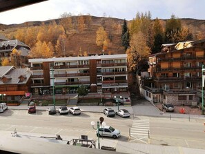 Un hotel de varios pisos con balcones, estacionamiento y montañas al fondo.