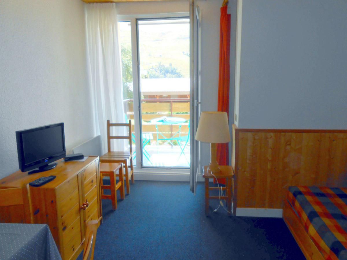 A hotel room with a television, wooden furniture, a table, chairs, a lamp, and a view of the outside balcony.
