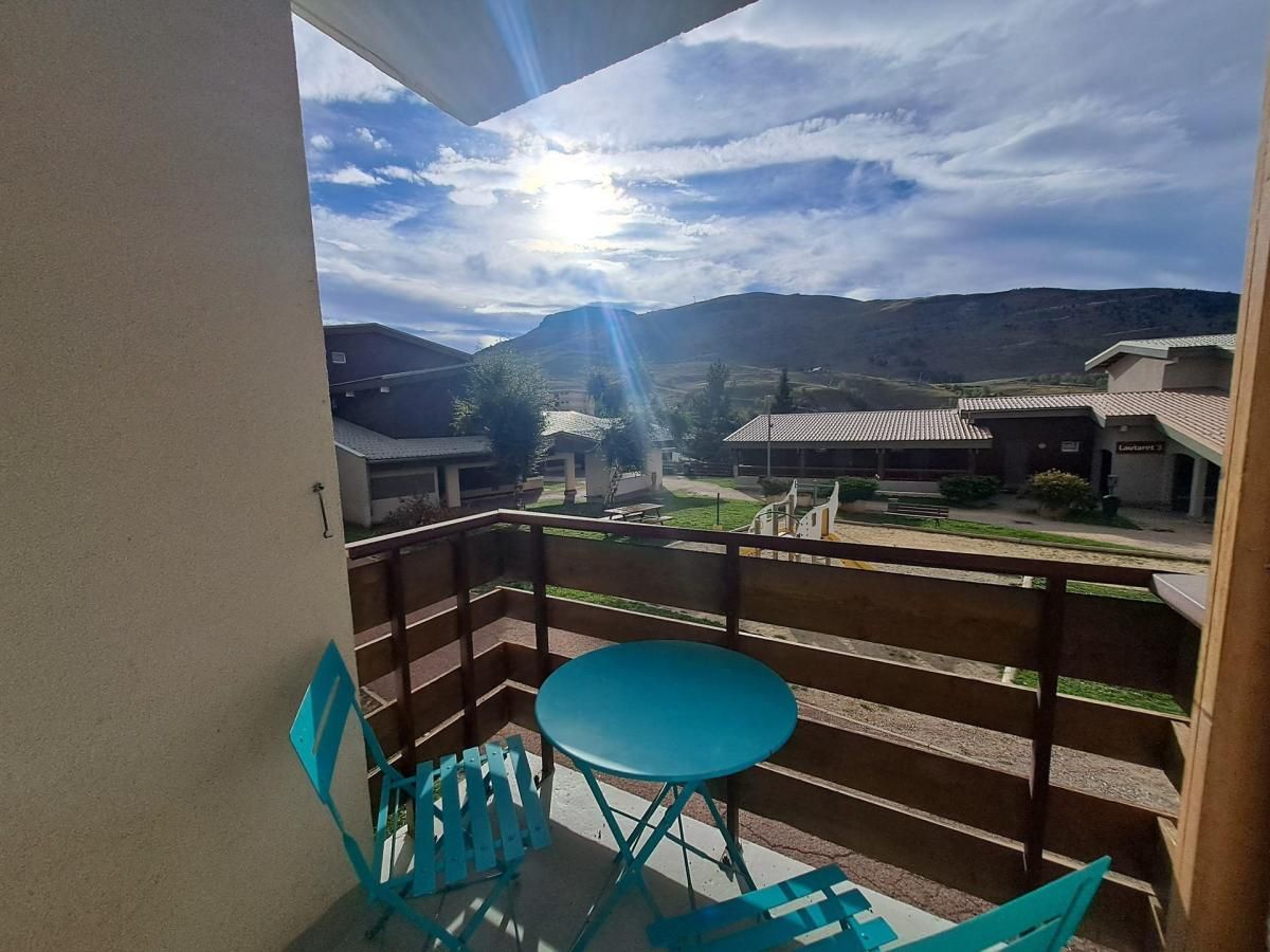 A balcony with a table and chairs, overlooking a courtyard with buildings and a mountain range.