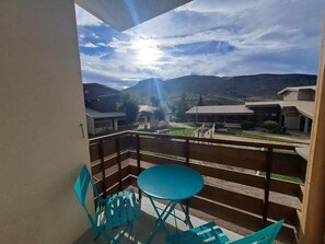 Un balcon avec une table et des chaises, donnant sur une cour intérieure bordée de bâtiments et sur une chaîne de montagnes.