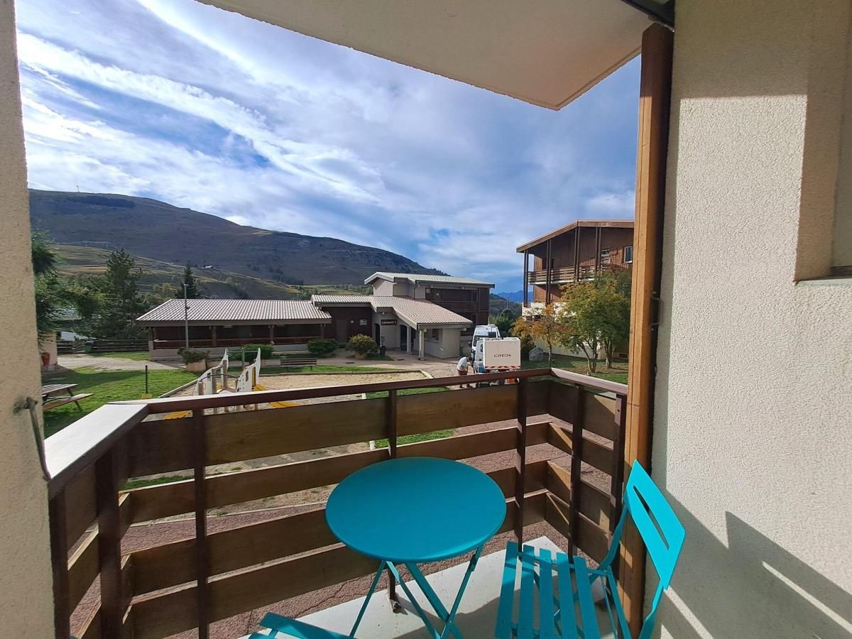 Un balcon avec une table et des chaises, d’où l’on peut admirer un immeuble et un paysage montagneux.