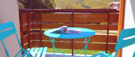 Een balkon met een tafel en twee stoelen, met uitzicht op een glooiend landschap.
