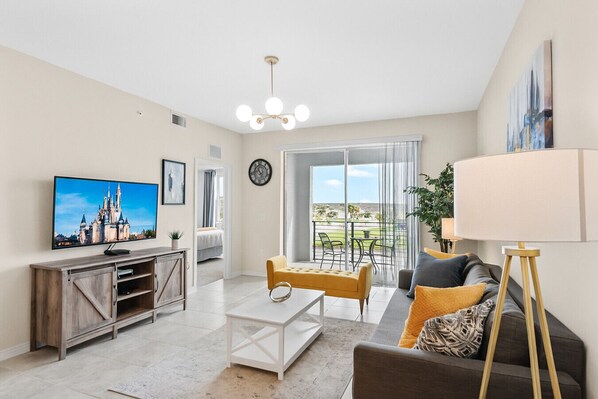 A modern living room with a flat-screen TV, a sofa, a coffee table, and a balcony with outdoor furniture.