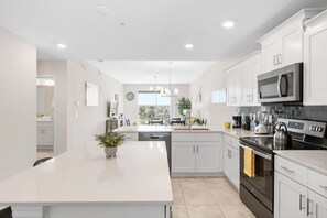 A modern kitchen with white cabinetry, a central island, stainless steel appliances, and a view to the outdoors.