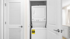 Un lavadero pequeño y blanco con lavadora y secadora integradas, una etiqueta visible de eficiencia energética, y una puerta con manija.