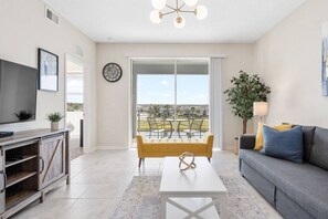 A modern living room with a sofa, a coffee table, a TV, and a balcony with outdoor furniture.