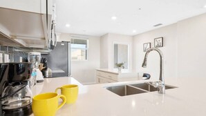 Una cocina moderna con un lavamanos doble, una cafetera y tazas amarillas sobre la encimera.