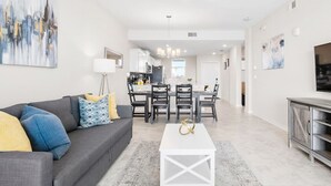 Uma sala de estar moderna com um sofá cinzento, uma mesa de centro branca e um espaço de jantar com mesa e cadeiras.