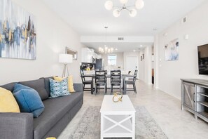 Una sala de estar moderna con un sofá gris, una mesa de centro blanca y un comedor con mesa y sillas.