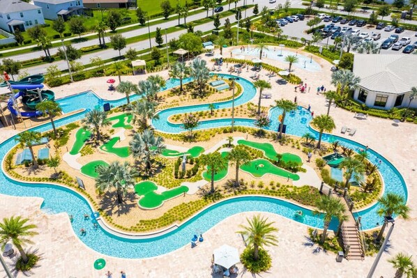 A golf course with multiple water hazards and a pool area with palm trees and lounge chairs.