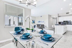 A modern dining area with a glass table, blue dinnerware, and a white orchid centerpiece.