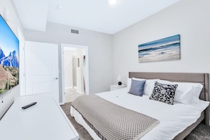 A modern hotel room with a large bed, a desk, and a painting of a beach scene.