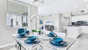 A modern dining area with a glass table, blue dinnerware, and a white orchid centerpiece.