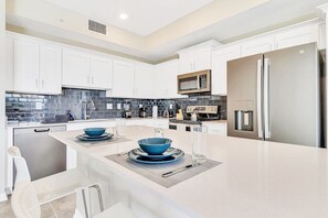 Una cocina moderna con armarios blancos, un refrigerador de acero inoxidable y una isla central con cuencos azules.
