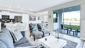 A modern living room with a grey sofa, a white coffee table, and a dining area with a bar.