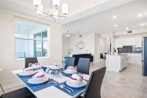 A modern dining area with a large table set for a meal, a kitchen in the background, and a view of the outdoors. - 3171-206 Resort Lake View Disney Universal Orlando (Kissimmee)