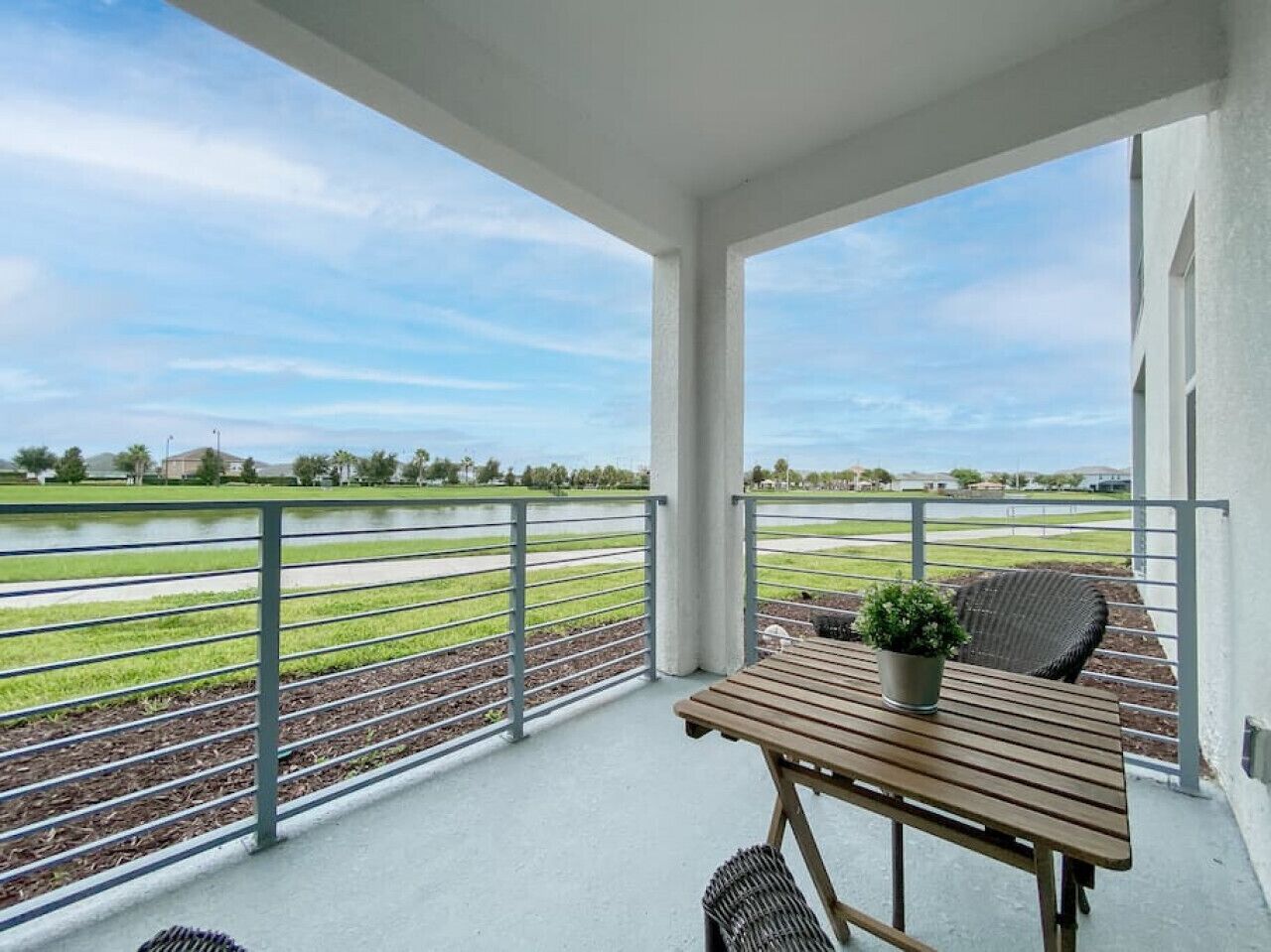 A balcony with a view of a sports field, a table, and a chair.