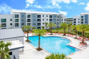 Ein modernes Hotel mit großem Pool, umgeben von Palmen und roten Liegestühlen.