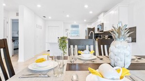 Un espace repas moderne avec une table en bois dressée pour deux personnes, des assiettes blanches, des verres transparents et un ananas décoratif en guise de centre de table.