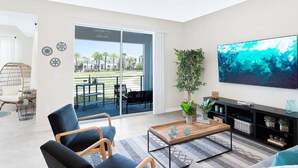 A modern living room with a large TV, comfortable seating, a balcony with a view, and a potted plant. - 3150-106 Resort Pool View Disney Universal Orlando (Kissimmee)