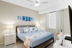 A bedroom with a bed, nightstands, a ceiling fan, artwork on the wall, and a window with curtains. - 3150-106 Resort Pool View Disney Universal Orlando (Kissimmee)