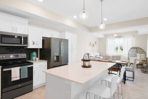 A modern kitchen with white cabinets, a black stove, stainless steel appliances, and a central island with bar stools.