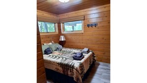 Une chambre dans une cabane en bois, avec un lit, deux fenêtres et une lampe.