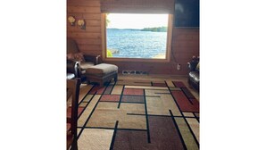 L’intérieur d’une cabane, avec une grande fenêtre donnant sur un lac, un tapis à motifs et des meubles en bois.