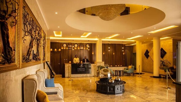 A luxurious lobby with a reception desk, plush seating, and a chandelier. - OMEDEL LUXURY (Enugu)