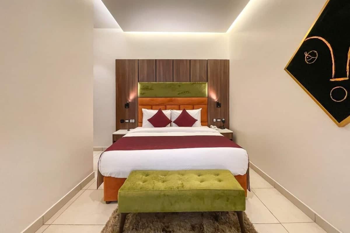 A modern bedroom with a large bed, a green ottoman, and a unique wall art piece.